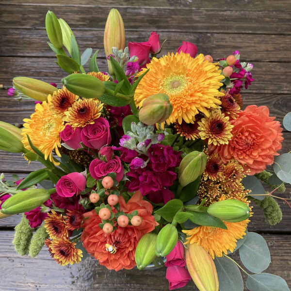 Bright mixed bouquet with yellow daisies, pink roses, orange blooms, and lily buds