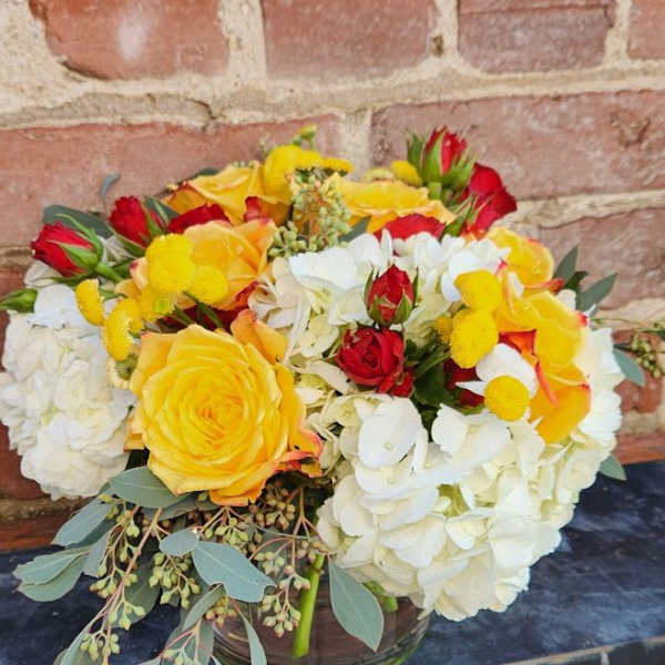 Low arrangement of white hydrangeas with yellow and red roses in a clear glass vase