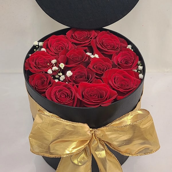Black round gift box filled with red roses and a gold bow