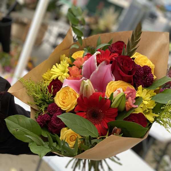 Mixed bouquet of roses, lilies, and daisies wrapped in brown paper