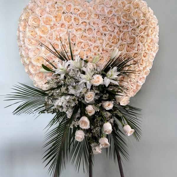 Heart-shaped floral spray of pale peach roses with white lilies and palm fronds