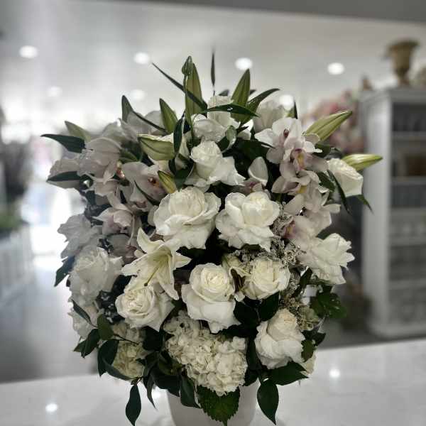 White floral arrangement in a white vase with roses and lilies