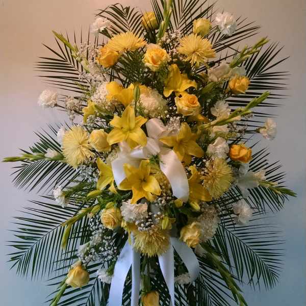 Standing floral spray with yellow lilies and roses on a white ribboned easel