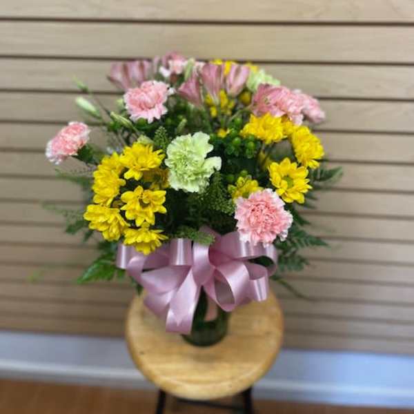 Bouquet of yellow and pink flowers tied with a pink ribbon in a vase