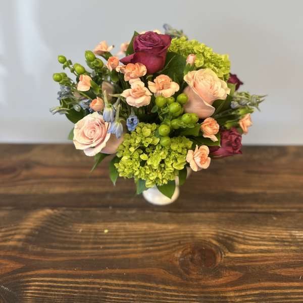 Compact arrangement of pink roses, peach carnations, green hydrangea, and berries in a white vase