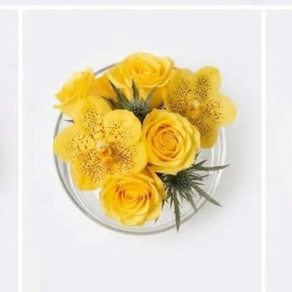 Yellow roses and orchids arranged in a clear round vase