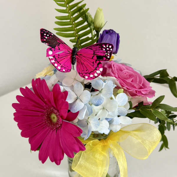 Bouquet of pink and white flowers in a glass vase with a yellow ribbon and butterfly decoration