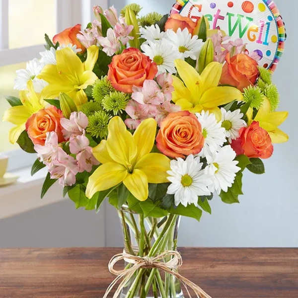 Mixed bouquet of yellow lilies, orange roses, and white daisies in a glass vase
