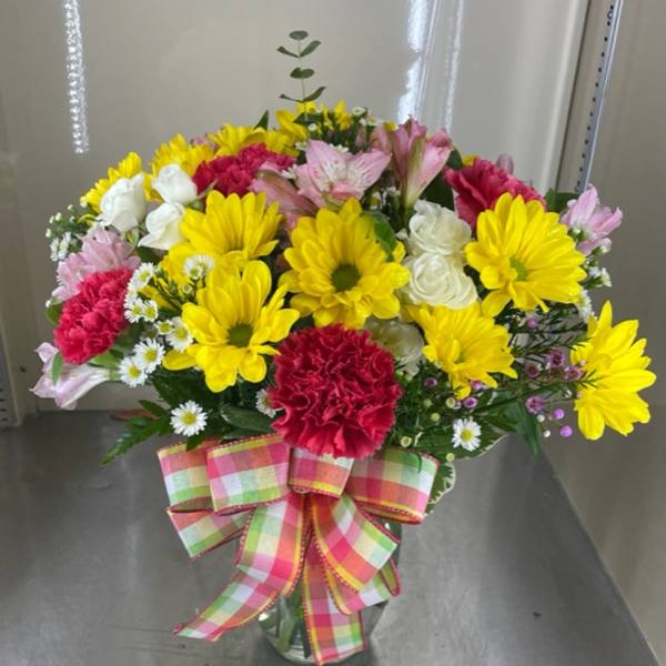 Mixed bouquet of yellow daisies, pink carnations, and white roses in a glass vase