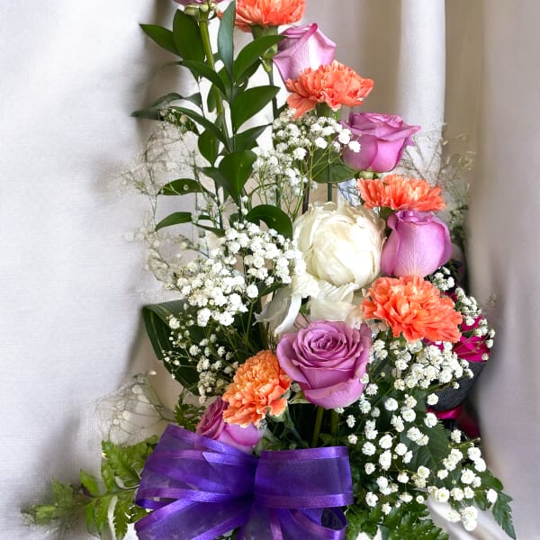 Bouquet of purple roses, orange carnations, and white flowers with a purple ribbon