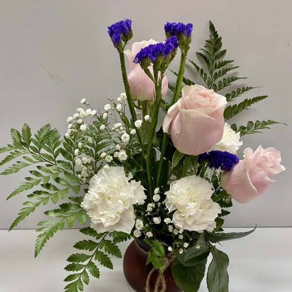 Pink roses and white carnations in a small vase with purple filler flowers