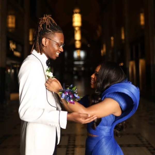 Couple in formal attire exchanging a boutonniere in a dim hallway