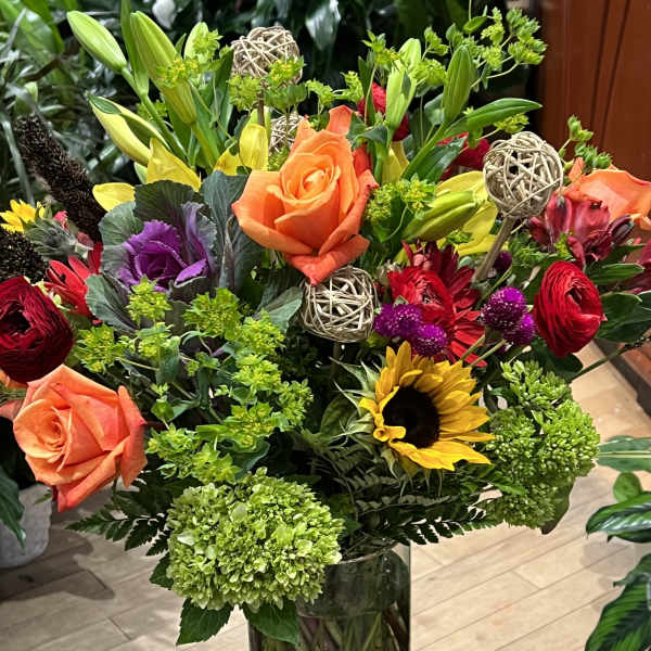 Mixed bouquet with roses, lilies, sunflowers, and hydrangeas in a glass vase