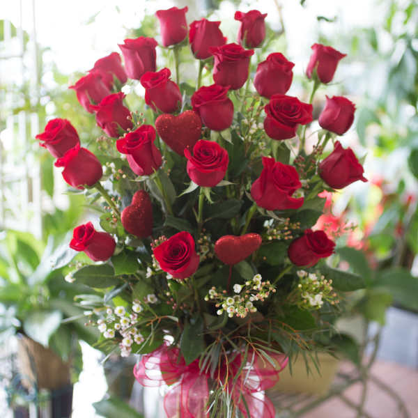 Red roses in a clear glass vase with glittery heart picks