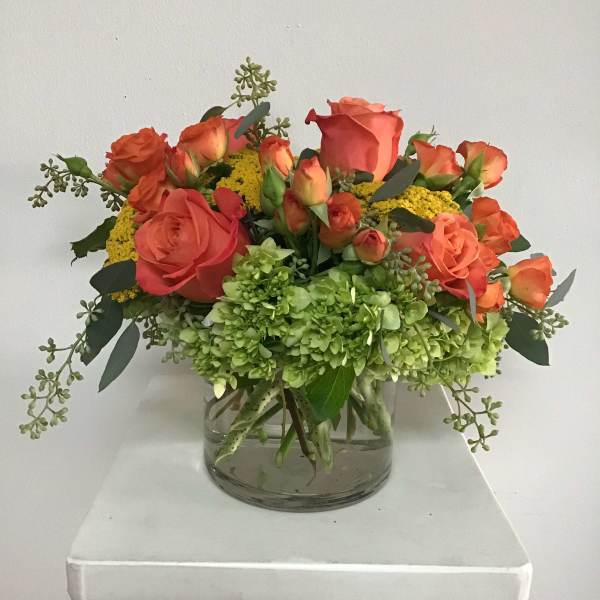 Orange roses and green hydrangeas in a clear glass vase