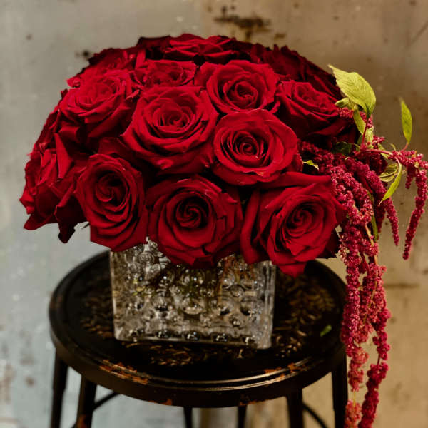 Red rose bouquet in a square glass vase with trailing pink accents