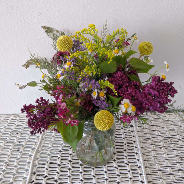 Mixed bouquet in a clear glass jar with purple, yellow, and white blooms