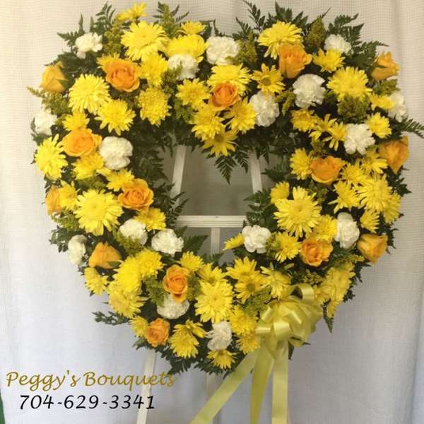 Heart-shaped yellow and white floral wreath on a stand with ribbon