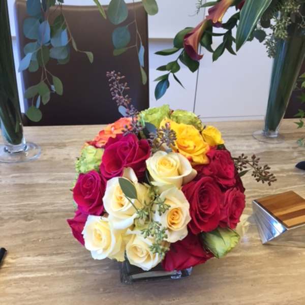Round bouquet of multicolored roses in a low square vase