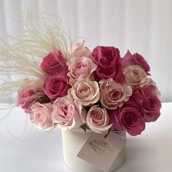 Pink and blush roses arranged in a round box with decorative grass