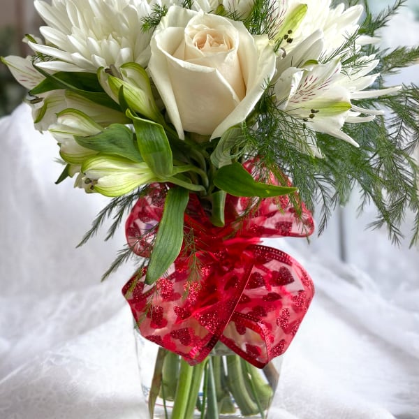 White rose and lily bouquet in a glass vase with a red ribbon