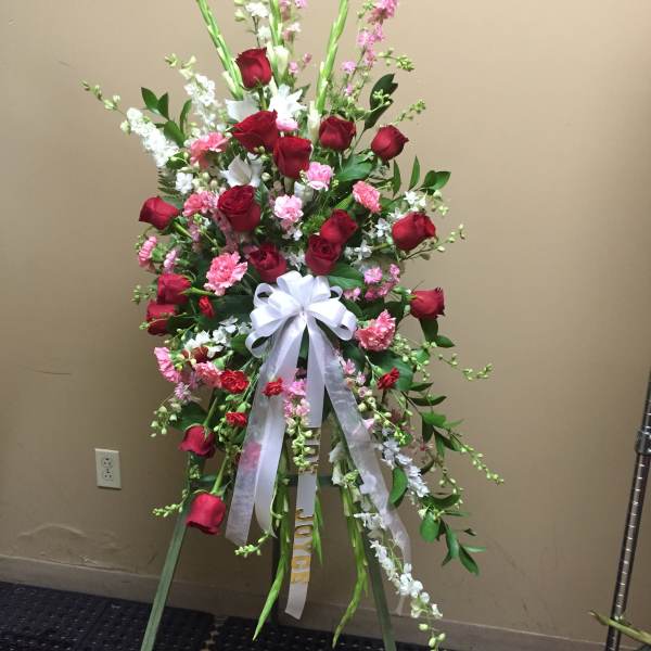 Standing spray of red roses, pink carnations, and white flowers with a white ribbon