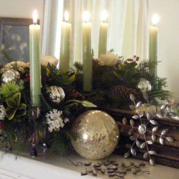 Holiday candle centerpiece with greenery and ornaments on a mantel