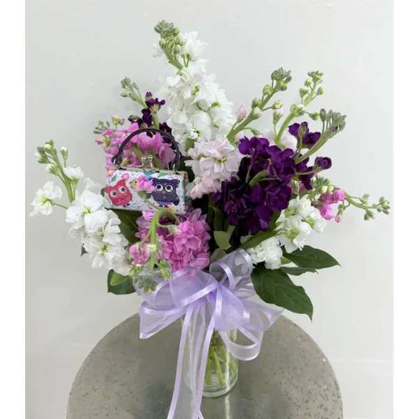Pink, white, and purple flowers in a glass vase with a lavender ribbon