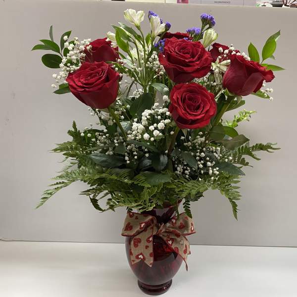 Red roses in a burgundy vase with baby's breath and greenery