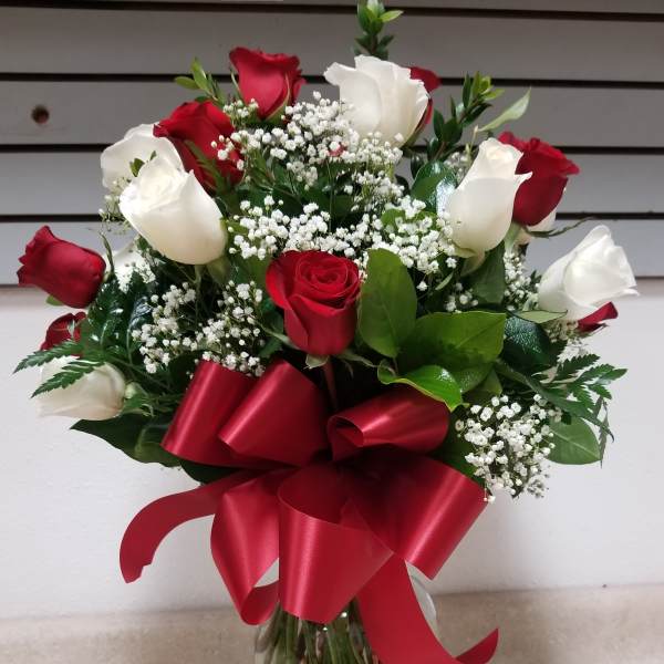 Red and white roses in a glass vase with a red ribbon