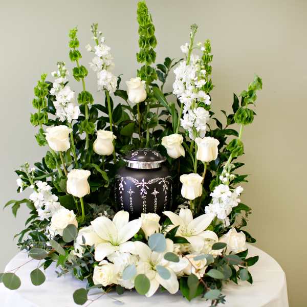 White roses and lilies surrounding a decorative urn in a tall white sympathy arrangement