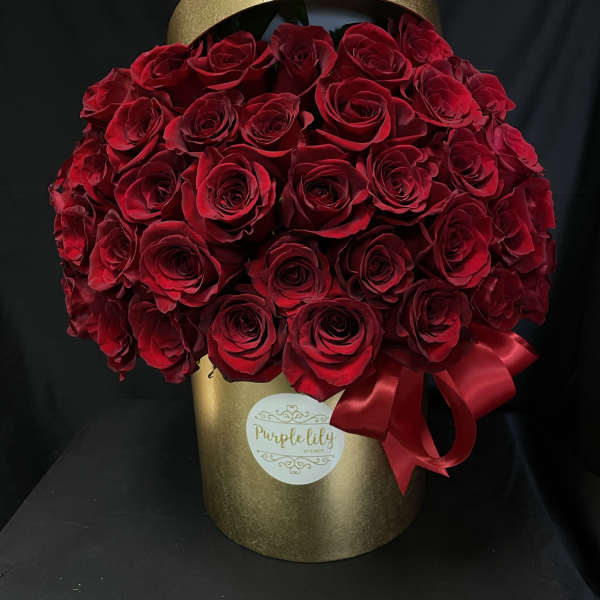 Red roses arranged in a gold hatbox with a red ribbon