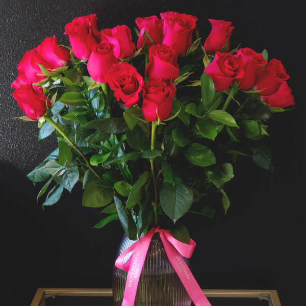 Bouquet of red roses in a ribbed glass vase with a pink ribbon