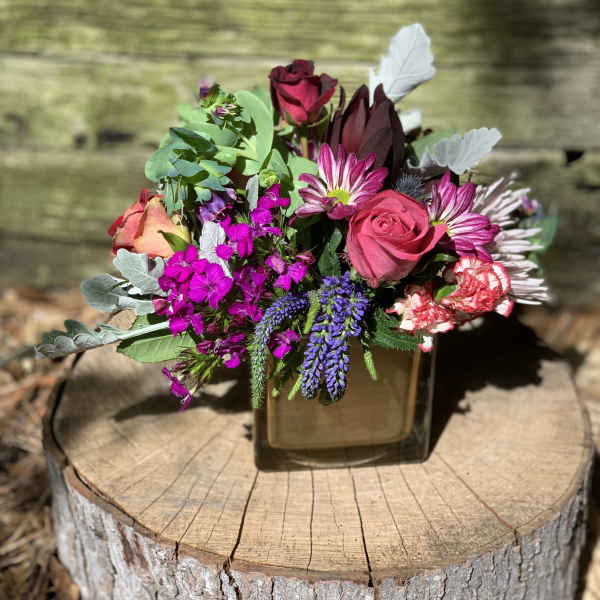 Mixed bouquet with pink roses, purple blooms, and a square glass vase