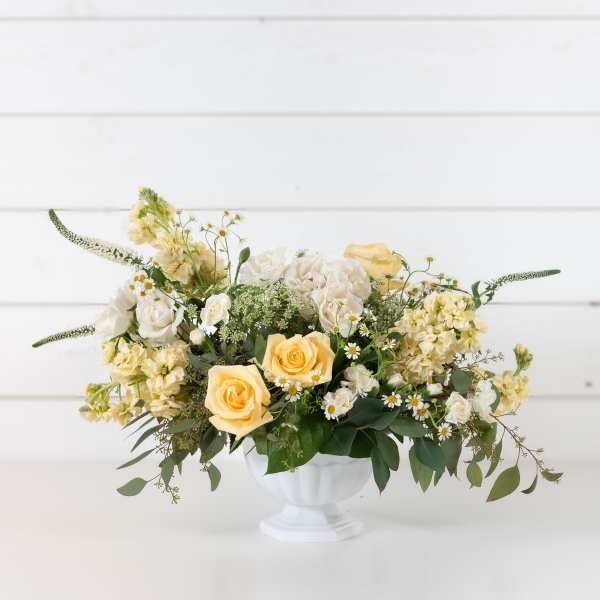 Cream and yellow floral arrangement in a white pedestal vase