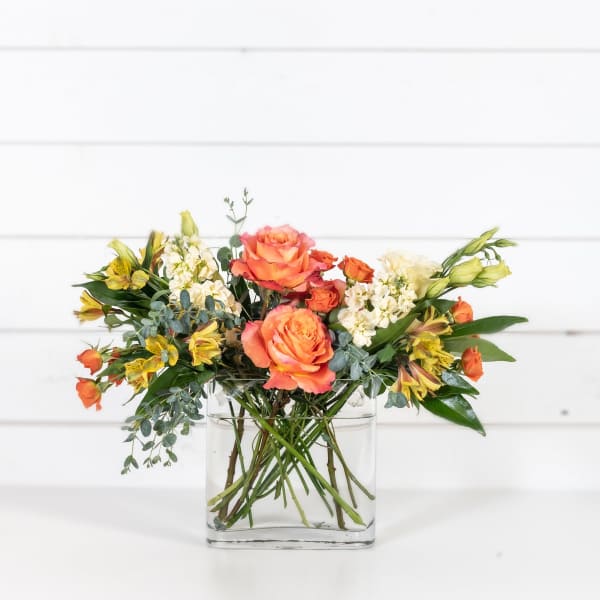 Orange roses and yellow alstroemeria in a clear glass vase