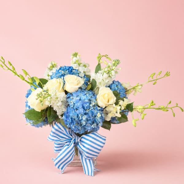 Blue hydrangea and white rose bouquet in a glass vase with a striped ribbon