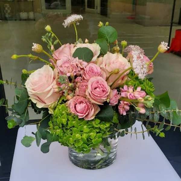 Low arrangement of pink roses and spray roses with bright green hydrangea in a clear glass vase