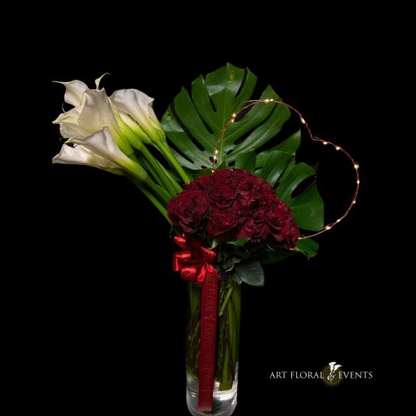 Bouquet of white calla lilies and deep red roses in a clear vase