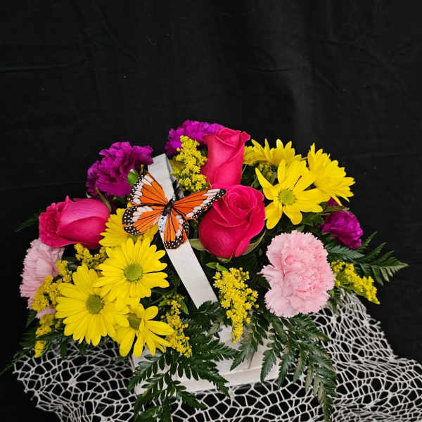 Pink roses and yellow daisies in a white basket with a butterfly decoration