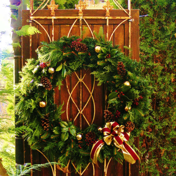 Evergreen wreath with pinecones and a red-and-gold bow on a wooden gate