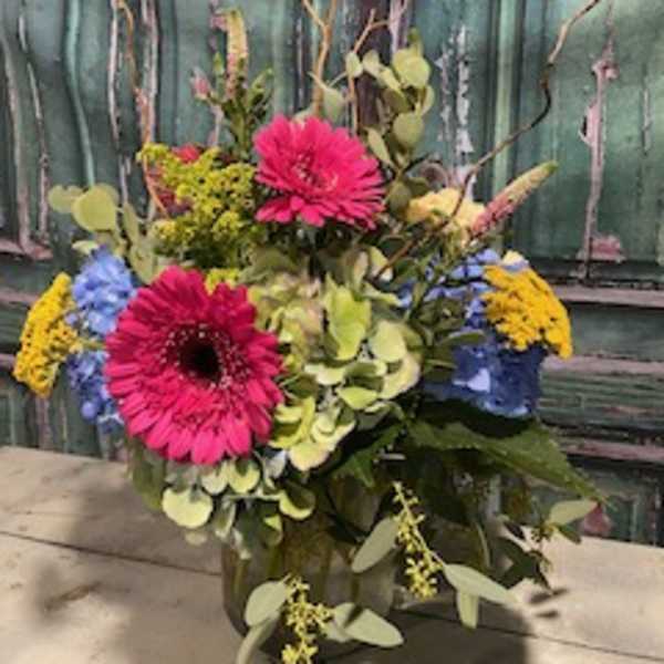 Bright mixed bouquet with pink gerbera daisies and blue and yellow blooms in a vase