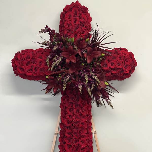 Cross-shaped floral tribute made of red roses with dark accent flowers