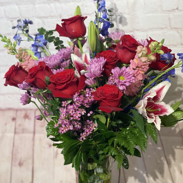 Bouquet of red roses, pink lilies, and purple flowers in a glass vase