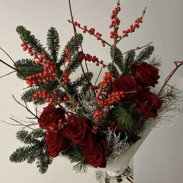 Red roses and berry branches in a clear glass vase
