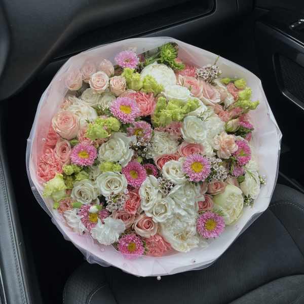 Large bouquet of pink, white, and green flowers wrapped in pale pink mesh