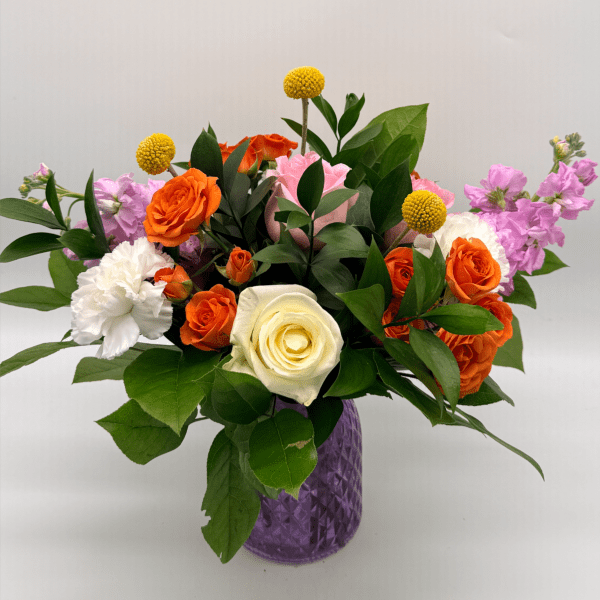 Colorful arrangement of orange roses, white rose and carnation, and pink blooms in a purple glass vase
