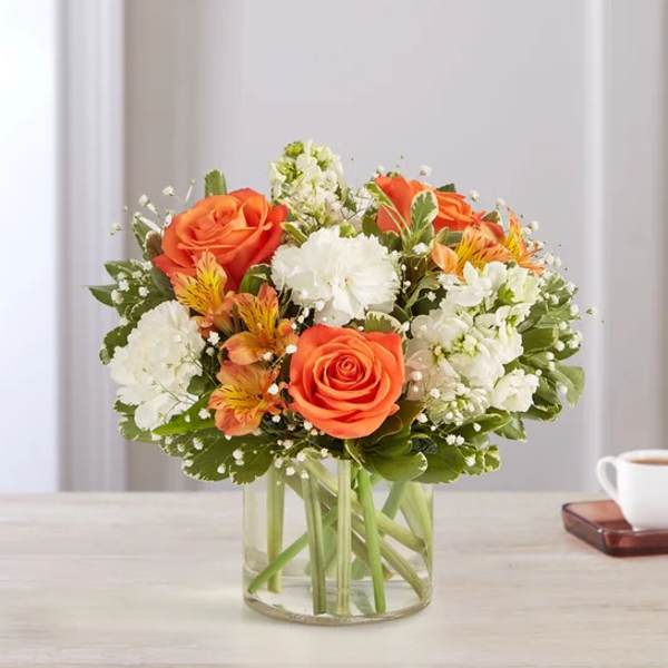 Orange roses and white flowers arranged in a clear glass vase