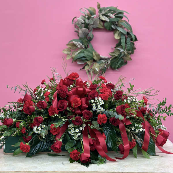Large red rose arrangement with ribbons and a leafy wreath above