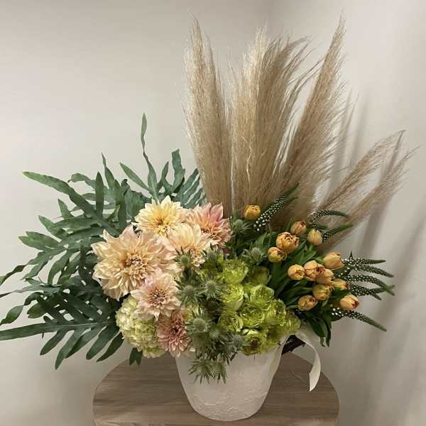 Tall asymmetrical arrangement with peach dahlias, green blooms, yellow tulips and pampas plumes in a white pot